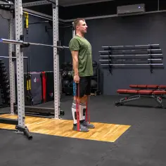 Mężczyzna w zielonej koszulce wykonuje ćwiczenie RDL (Romanian Deadlift) z gumą oporową.