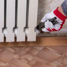 Ręka w rękawicy z kluczem nastawnym przyłącza grzejnik aluminiowy. Dowiedz się, jak rozkręcić grzejnik aluminiowy.