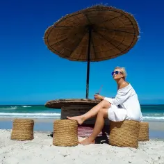 Kobieta w białej sukience siedzi pod parasolem na plaży na Djerbie. Uważać na słońce i upał.