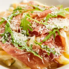 Penne z kremowym sosem, szynką parmeńską, rukolą i parmezanem. Pyszne makaronowe danie.
