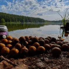 Słońce odbija się w spokojnej tafli jeziora, a na brzegu leżą przynęty wafters.