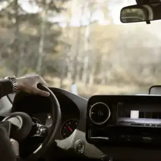 Mężczyzna za kierownicą, myślący o różnych kategorie prawa jazdy, podczas jazdy przez jesienny krajobraz.