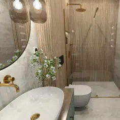 Nowoczesna łazienka z prysznicem wyłożonym pionowymi **lamele w łazience**. Złote baterie i detale dodają elegancji.