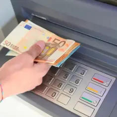 Dłoń trzyma banknoty 50 euro przy bankomacie. W Hiszpanii obowiązuje euro, więc to typowa waluta do wypłaty.