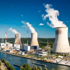 Widok elektrowni atomowej z chłodniami kominowymi, rzeką i otaczającą zielenią.