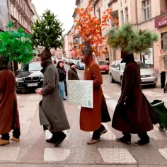 Ludzie w płaszczach i z drzewami na głowach przechodzą przez pasy. happening co to?