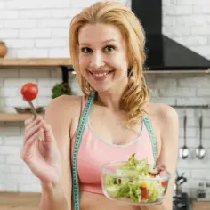 Uśmiechnięta kobieta z miarką krawiecką na szyi trzyma miskę sałatki i pomidorka. Idealna na dieta wysokobiałkowa jadłospis na 7 dni.