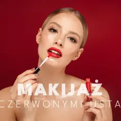 Kobieta zmysłowo maluje swoje czerwone usta błyszczykiem. Makijaż podkreśla jej urodę.