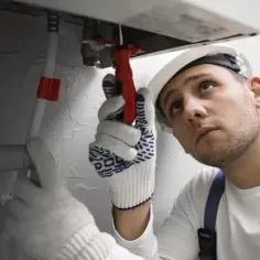 Instalator w białej rękawicy dokręca śrubę przy bojlerze.
