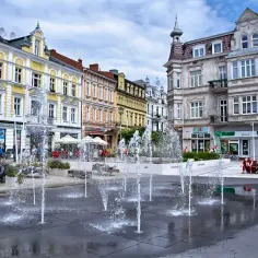 Urokliwy plac z fontannami w świnoujście stare miasto. Kolorowe kamienice, ludzie odpoczywający na ławkach i letnia atmosfera.
