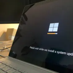 Ekran laptopa z logo Windows i komunikatem "Please wait while we install a system update". Aktualizacja systemu, która może obejmować sterowniki, jest w toku.