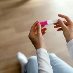 Dłonie trzymające test ciążowy. Czy ból sutków przed okresem to pierwszy sygnał?