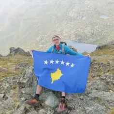 Mężczyzna z flagą Kosowa na szczycie górskim. Czy Kosowo jest bezpieczne? Widok zapiera dech w piersiach.