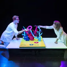 Dwoje aktorów w białych strojach tworzy magiczny świat na scenie. To teatr bajka Warszawa, gdzie kolorowe drzewka i pierścienie ożywają.