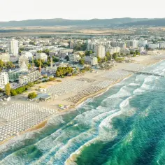 Słoneczna plaża z rzędami leżaków i parasoli, hotele i wesołe miasteczko. Ceny w Bułgarii zachęcają do wypoczynku nad morzem.