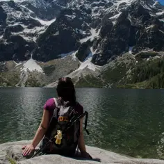 Widok na Morskie Oko z perspektywy turystki. Majestatyczne rysy gór otaczają taflę jeziora.