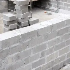 Ściana z bloczków fundamentowych w trakcie budowy. Widać stosy bloczków, gotowe fragmenty muru i materiały budowlane.