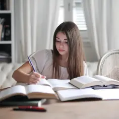 Dziewczyna pochylona nad książkami, pisząca piórem. To właśnie co to jest edukacja – zdobywanie wiedzy i rozwijanie się.