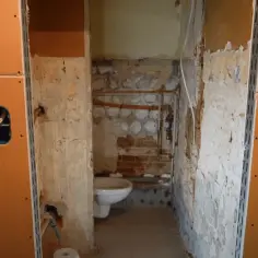 Remont łazienki w toku. Widać białą muszlę klozetową i instalacje. Ściany przygotowane pod płytę GK do łazienki.