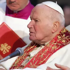 Papież Jan Paweł II w białej szacie z ozdobnym kołnierzem, podczas modlitwy o uzdrowienie.