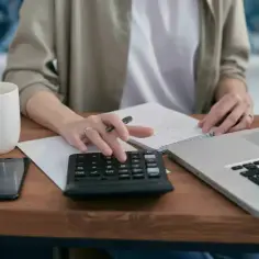 Osoba liczy na kalkulatorze, analizując, co obejmują składki ZUS. Na biurku laptop, telefon i kubek kawy.