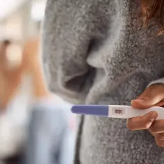 Kobieta trzyma test ciążowy z dwoma kreskami. Czy po okresie są dni niepłodne? To pytanie nurtuje wiele osób.