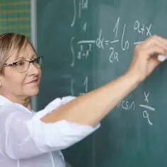 Nauczycielka matematyki pisze wzory na tablicy. Dziś godzina czarnkowa zniesiona, więc lekcja przebiega sprawnie.