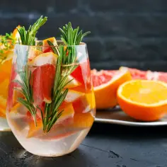 Orzeźwiający drink z grejpfrutem, pomarańczą i rozmarynem. Dwa szklane kieliszki wypełnione wodą, owocami i ziołami.