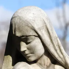 Kamienna rzeźba przedstawia smutną twarz kobiety w welonie, przypominającą św. Amelię, patronkę.