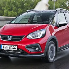 Czerwony Honda Fit w wersji Cross, z kroplami deszczu na karoserii, jedzie po mokrej drodze.
