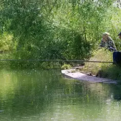 Dwoje wędkarzy, mężczyzna i kobieta, siedzi nad zieloną wodą, ciesząc się spokojem i techniką casting spinning.