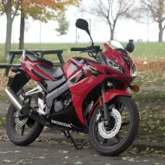 Czerwona Honda CBR 125R, gotowa do jazdy, z widocznym napisem "HONDA" na owiewce. Idealna na pierwsze wrażenia z jazdy, choć nie osiąga v-max jak jej więksi bracia.