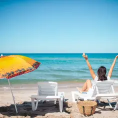 Kobieta cieszy się słońcem na plaży, marząc o tym, ile jest dni urlopu w roku. Obok parasol i leżaki.