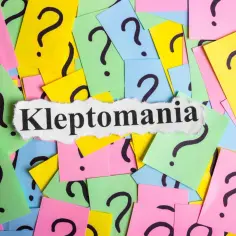 Klejnoty z napisem "Kleptomania" na tle kolorowych karteczek z pytajnikami.