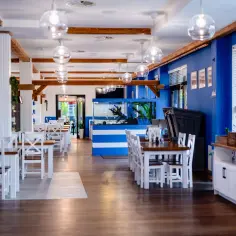 Wnętrze restauracji Papaj w Jastrzębiej Górze. Białe stoły i krzesła, niebieskie ściany, akwarium i drewniane belki tworzą nadmorski klimat.