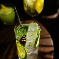Orzeźwiający drink z ogórkiem, miętą i wiśnią, z lodem i słomką. W tle inne napoje.