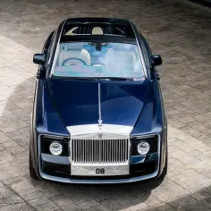 Ekskluzywny Rolls-Royce Sweptail w kolorze głębokiego granatu, z jasnym wnętrzem, prezentuje się majestatycznie na brukowanym podjeździe.