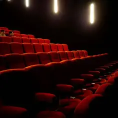 Czerwone fotele w kinie, widok na teatr Palladium plan widowni. Kilka osób siedzi w pustej sali.