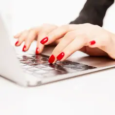 Dłonie z czerwonymi paznokciami piszą na laptopie. Czy pracodawca czyta maile pracowników? Prywatność w miejscu pracy to ważna kwestia.