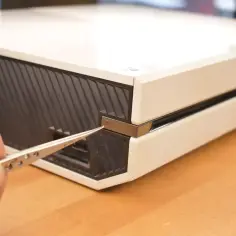 Dłoń z pęsetą zbliża się do przycisku parowania Xbox One, aby połączyć kontroler.