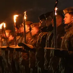 Żołnierze w czapkach typu capstrzyk niosą pochodnie podczas nocnej uroczystości.