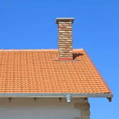 Ceglany komin na dachu z dachówki. Zastanawiasz się, ile kosztuje obróbka komina blachą?