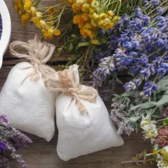 Dwa lniane woreczki z suszoną lawendą, której zapach zawdzięcza linalool, otoczone bukietami ziół i kwiatów.