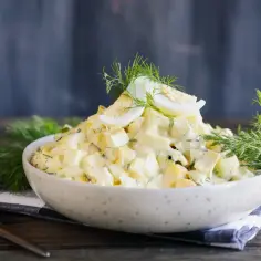 Sałatka jajeczna z koperkiem w misce, udekorowana jajkiem na twardo i gałązkami koperku.