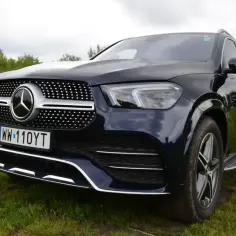 Ciemnoniebieski Mercedes GLE 450 na trawiastym polu, z widocznym grillem i reflektorami.