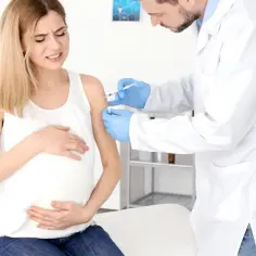 Lekarz podaje szczepionkę w ramię ciężarnej kobiety, która odczuwa ból. To ważna profilaktyka, by chronić ją i dziecko przed chorobami, np. jelitówką.