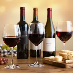 Degustacja win: porównanie smaku szczepów Cabernet Sauvignon i Merlot. Na stole kieliszki z czerwonym winem, butelki, ser i winogrona.