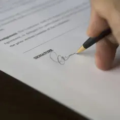 Dłoń z długopisem podpisuje dokument, co symbolizuje przedłużenie umowy najmu.