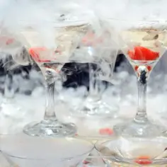 Efektowne drinki z suchym lodem tworzą mglistą, tajemniczą atmosferę. Kieliszki wypełnione są złotym płynem i ozdobione czerwonymi owocami.