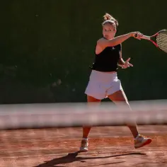 Tenisistka wykonuje potężny backhand na ceglanym korcie.